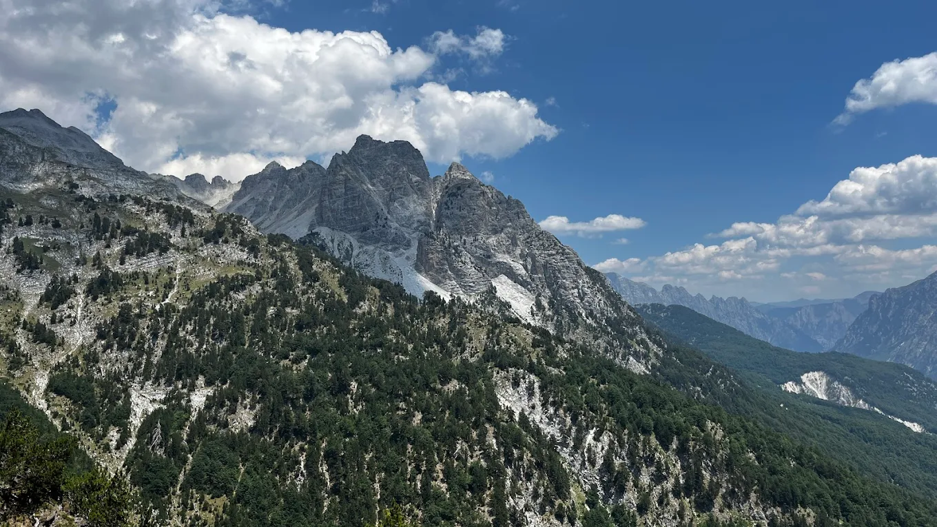 Scenic mountain landscape with rocky peaks and green forest under blue sky